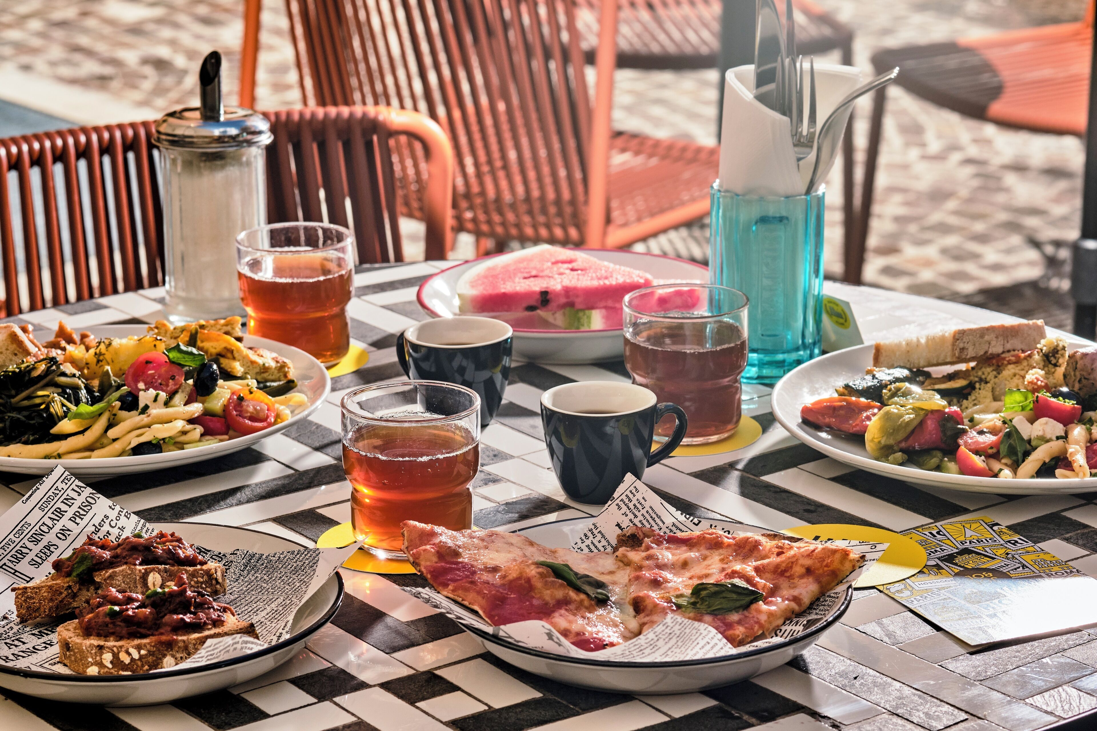 A table set with various dishes, drinks, and a newspaper.