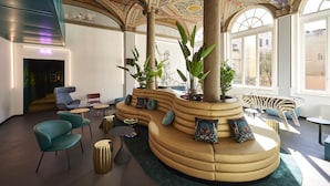 A modern lounge area with a curved sofa, seating, and a large plant.