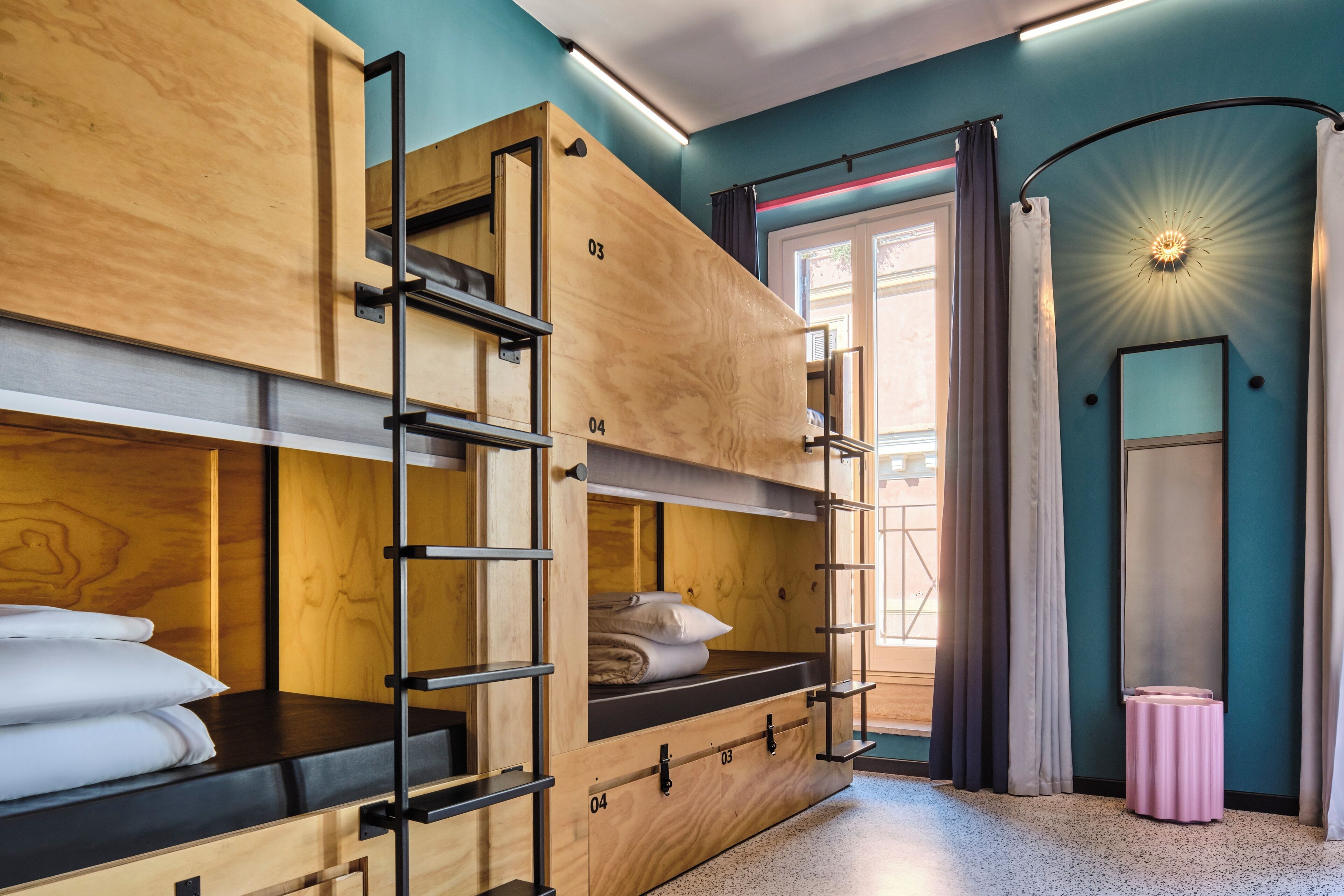 Dormitorio con literas, una escalera de madera, una mesita y una ventana con cortinas.