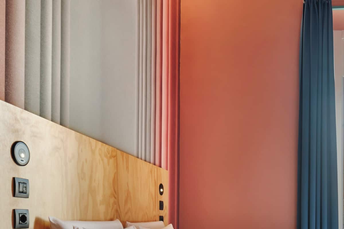 Ein Hotelzimmer mit Holz-Kopfteil, einem Bett mit weißer Bettwäsche, einem Nachttisch und einem blauen Vorhang.