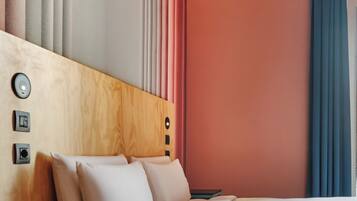 A hotel room with a wooden headboard, a bed with white bedding, a nightstand, and a blue curtain.