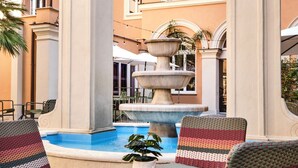 An outdoor seating area with a fountain, umbrellas, and a pool.