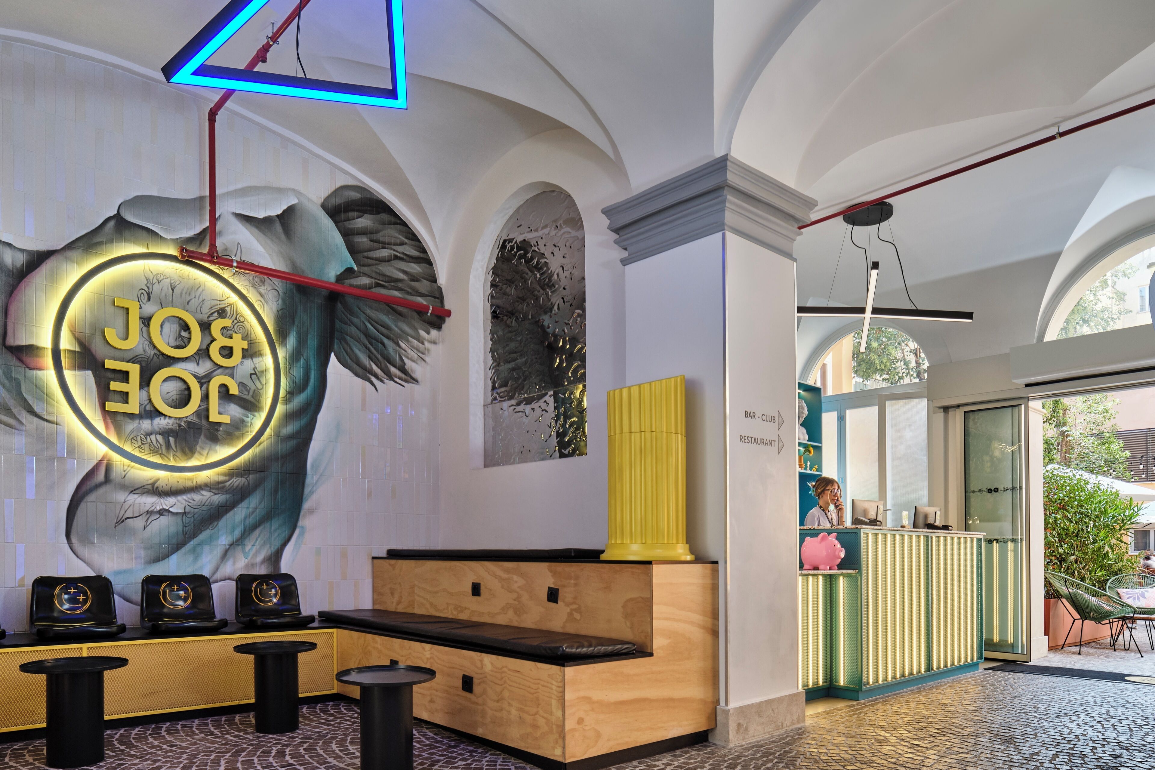 Un espace d’accueil agrémenté d’une grande fresque murale, d’un banc en bois et d’un panneau lumineux au néon.