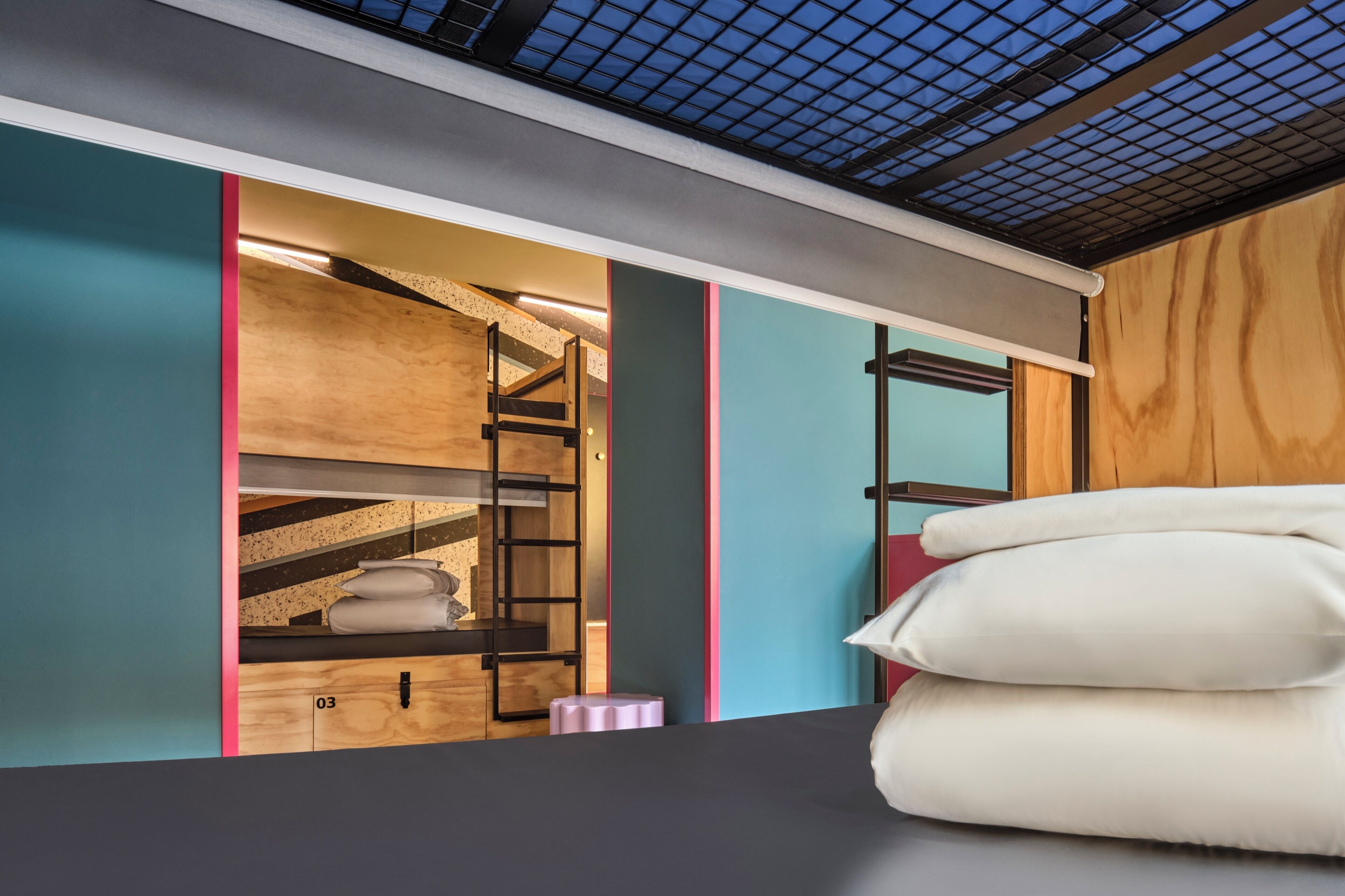 A bunk bed with a wooden ladder, a small pink stool, and a white pillow on a dark-colored bed.