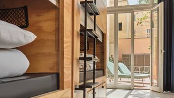 Habitación compacta con literas, un escritorio pequeño y una puerta corrediza de vidrio que da a un área de estar al aire libre.