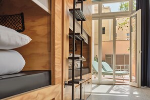 A compact room with a bunk bed, a small desk, and a sliding glass door leading to an outdoor seating area.