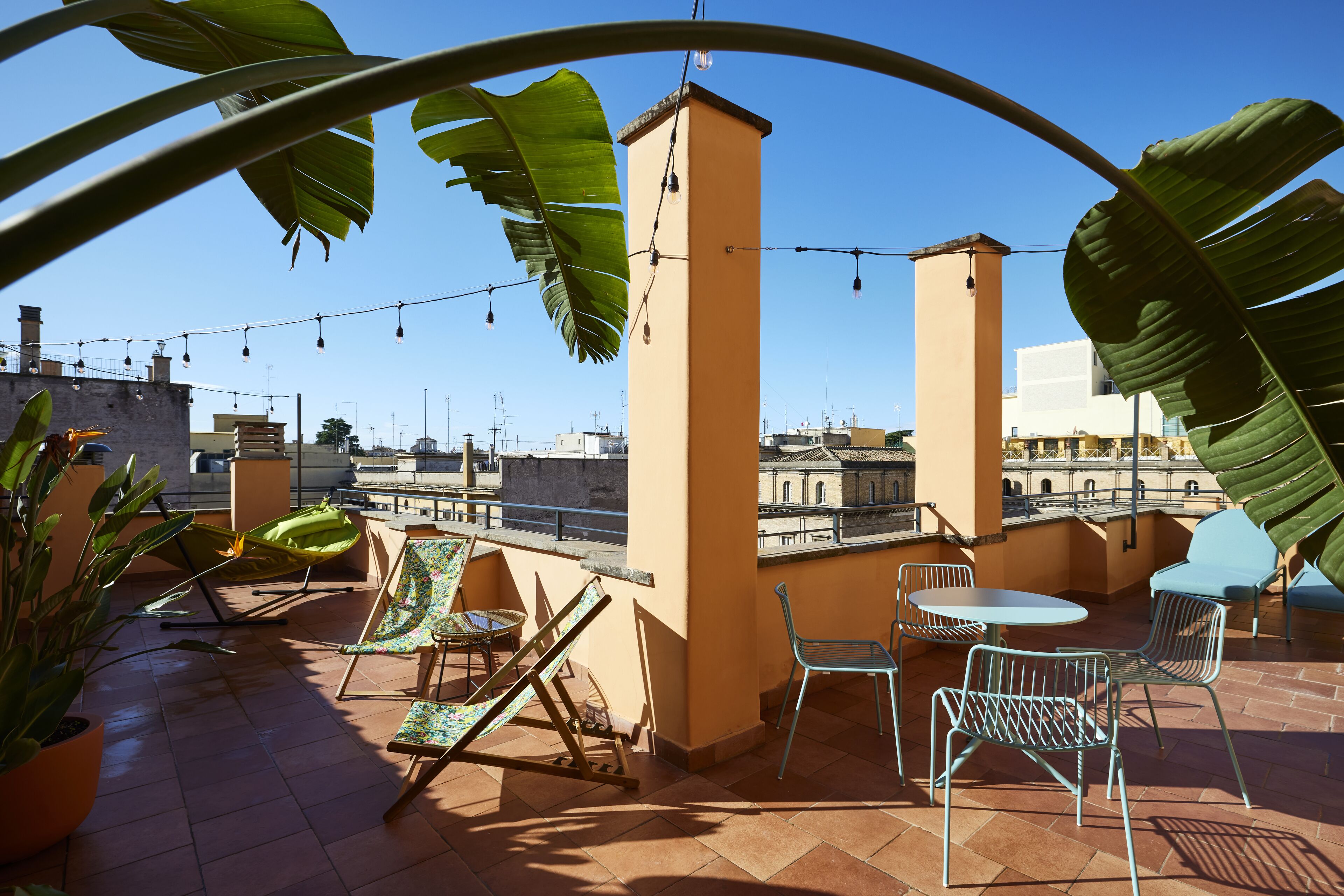 Una terrazza sul tetto con vista chiara sulla città, con tavolo e sedie, piante in vaso e luci decorative.