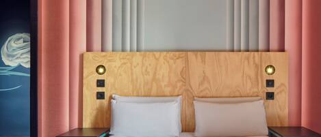 Una habitación de hotel moderna con cabecera de madera, dos almohadas blancas y una mesita de noche con lámpara.