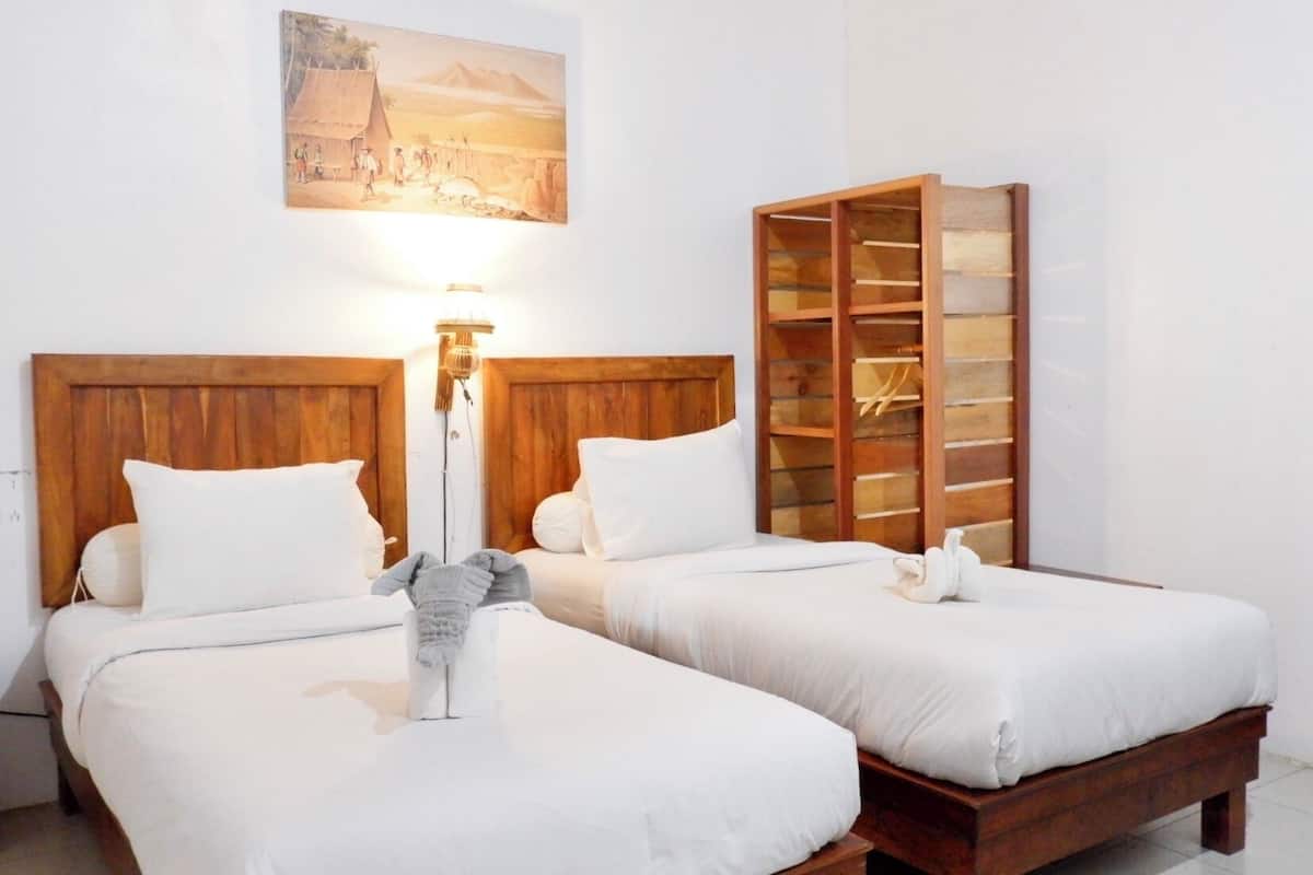 Een hotelkamer met twee bedden, een houten hoofdbord, een wandlamp en een plank met spullen.