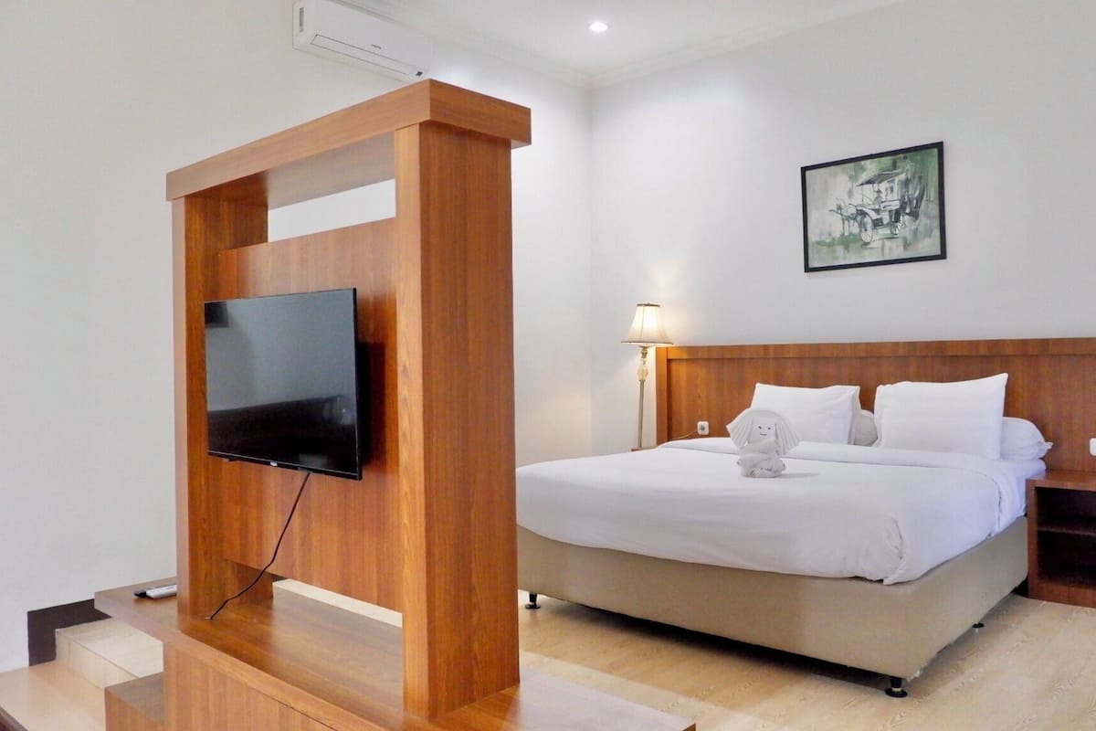 Een hotelkamer met een bed, een aan een houten constructie bevestigde televisie, een nachtkastje en een wandlamp.