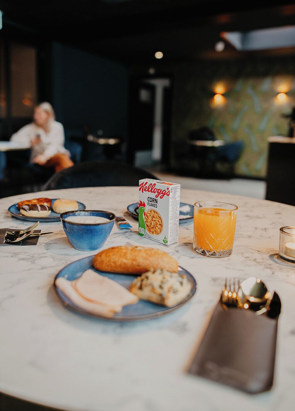 Un desayuno con un bol de cereal, un vaso de zumo de naranja y una hogaza de pan sobre una mesa de mármol.