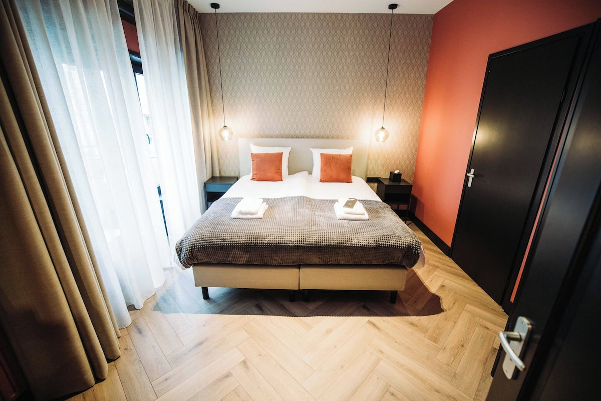 Una habitación de hotel con una cama grande, dos mesitas de noche, un armario y un suelo con estampado de espiga.