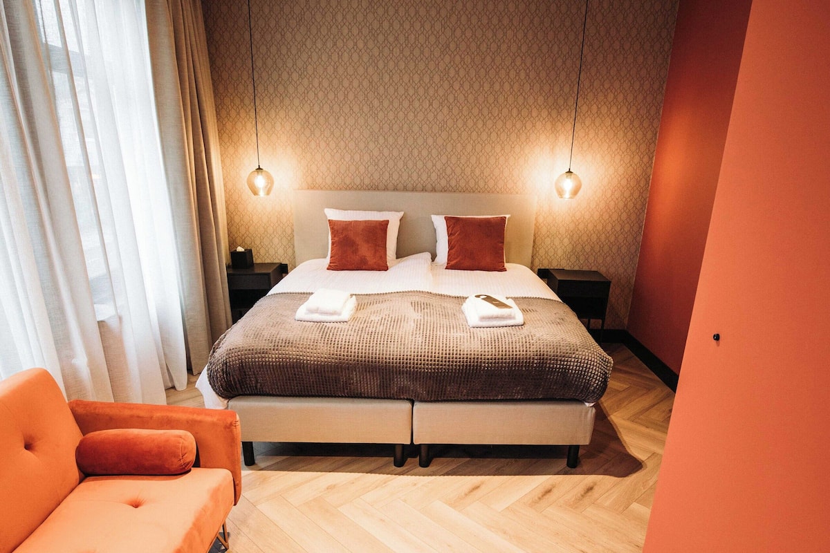 Una habitación de hotel moderna con una cama grande, un sofá y un suelo de madera en espiga.