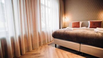 A hotel room with a large bed, wooden flooring, and a patterned wall.