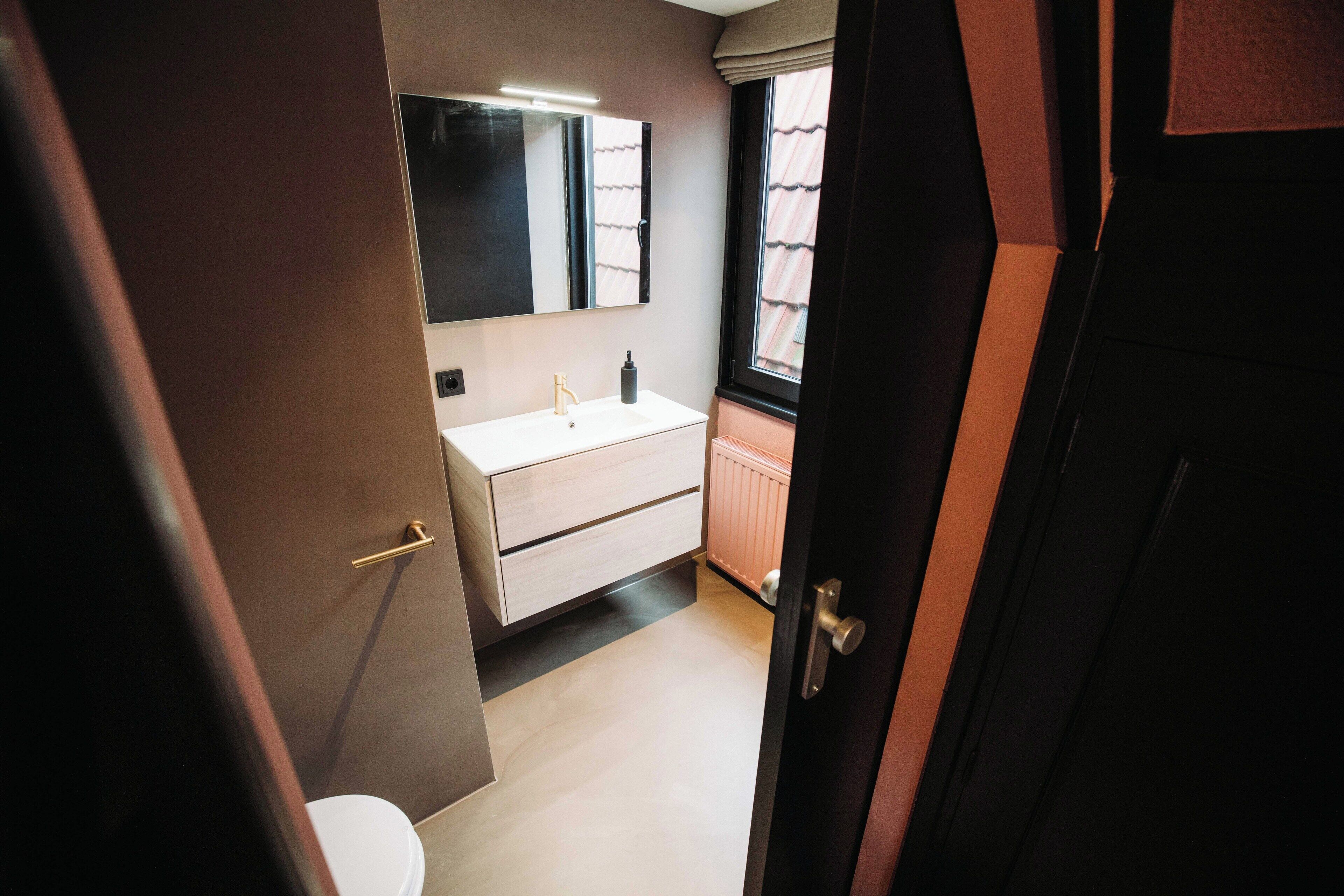 Een kleine badkamer met een wit wastafel, een spiegel en een raam.