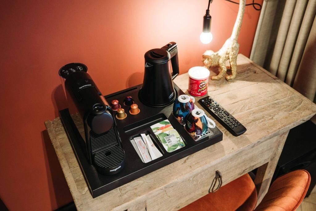 Une petite table avec une machine à café, des télécommandes, une petite figurine et quelques en-cas.