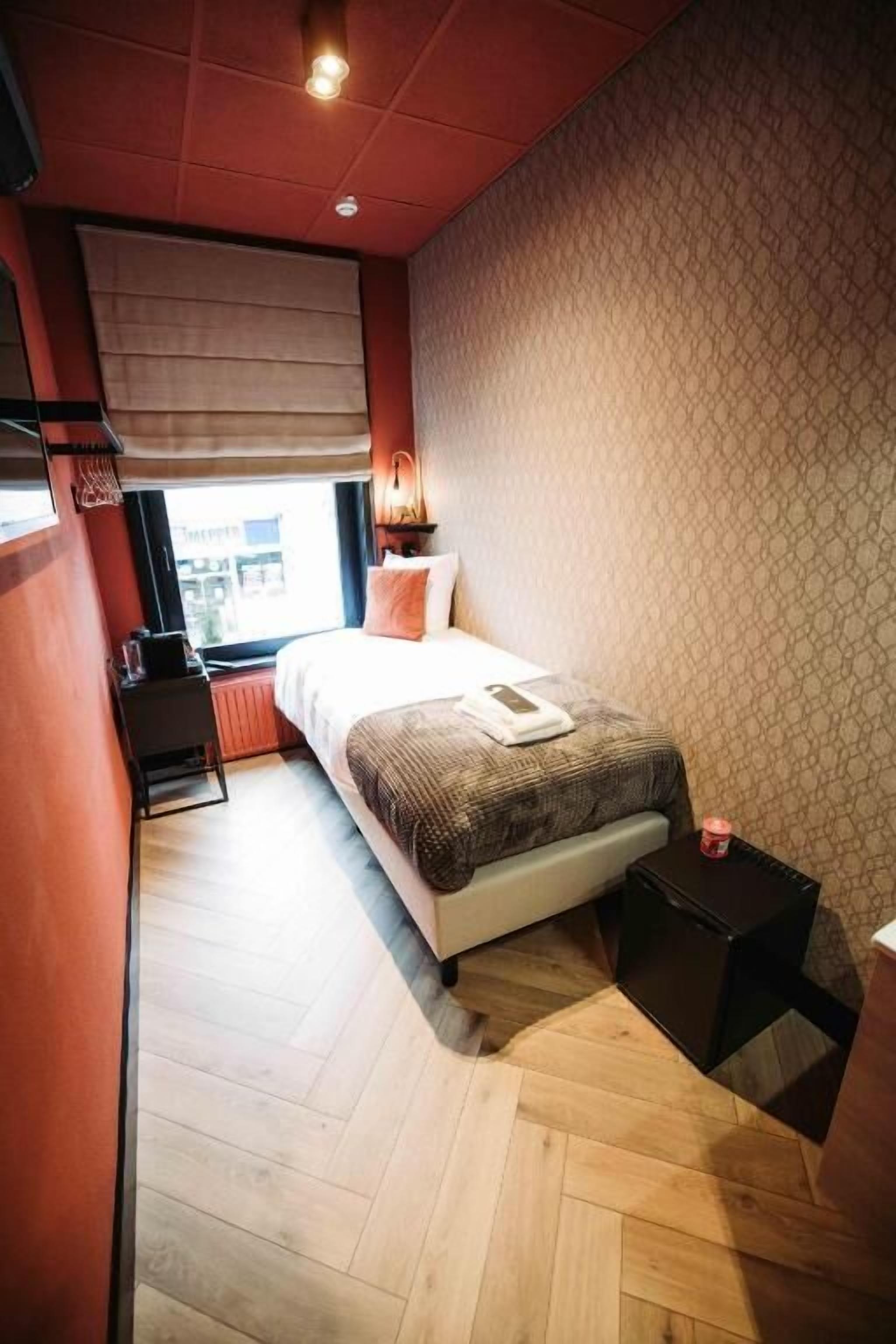 Una habitación de hotel pequeña con cama, mesita de noche y un escritorio con silla.