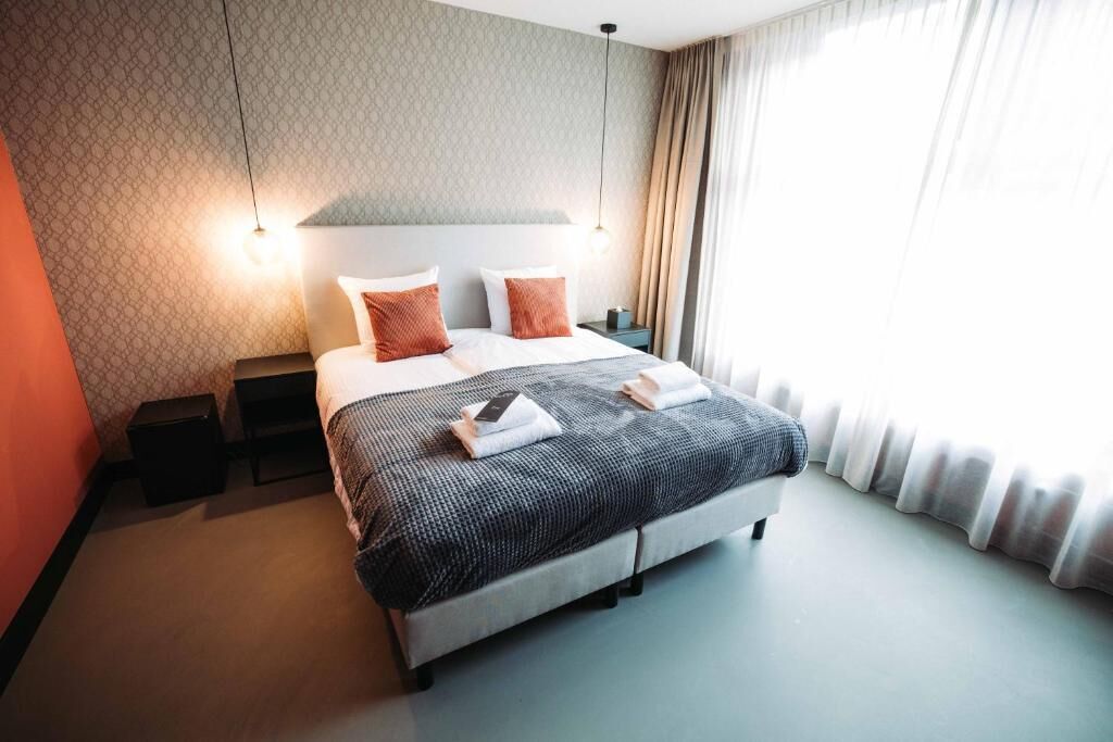 Moderni hotellihuone, jossa on suuri sänky, yöpöydät ja näkymä ulos.