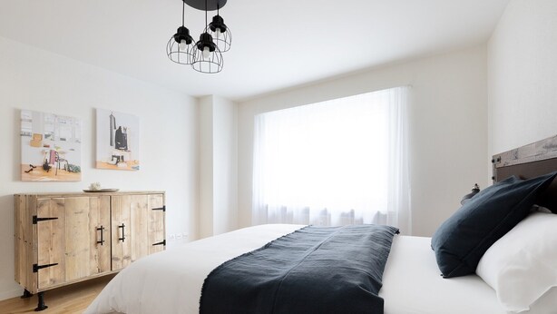 A bedroom with a bed, a wooden wardrobe, and a window with curtains. - Nest - Riehenring (Basel)