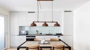 A modern kitchen with white cabinets, a wooden dining table, and two pendant lights. - Nest - Riehenring (Basel)