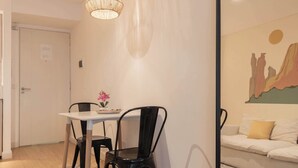 Un coin repas avec une table et des chaises, un luminaire suspendu, un tableau au mur et un canapé avec des coussins.