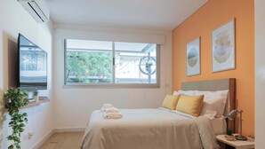 Une chambre à coucher avec un lit, une table de chevet avec une lampe, une fenêtre et un téléviseur fixé au mur.