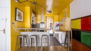 Une cuisine avec un mur jaune, une porte blanche et un coin bar avec des tabourets.