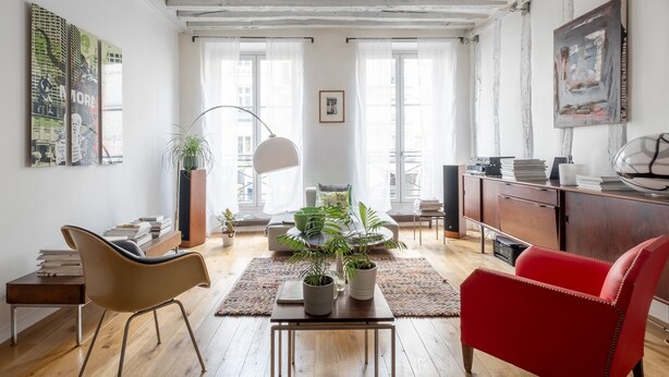 Un salon avec un plancher en bois, un fauteuil rouge, une table ornée de plantes et une bibliothèque.