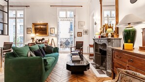 A spacious living room with a green sofa, a fireplace, and a large mirror. - Avenue Heights, by Veeve (Paris)