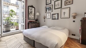 A bedroom with a large bed, a dresser, a mirror, and a window with a view of buildings. - Avenue Heights, by Veeve (Paris)