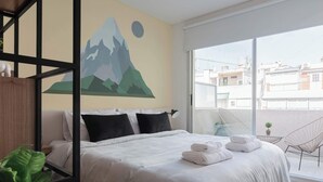 Ein modernes Hotelzimmer mit einem großen Bett, einem Wandbild von Bergen, einem Balkon mit Blick auf Gebäude und einem kleinen Tisch mit einer Pflanze.