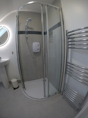 A modern bathroom with a glass-enclosed shower, a white sink, and a chrome towel rack. - Triple room with ensuite bathroom (Portmagee)
