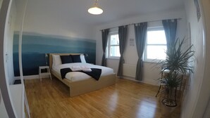 Una camera da letto con un letto, un comodino, una finestra con tende, una pianta in vaso e un affresco.