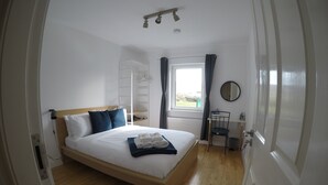 A bedroom with a wooden bed, a bedside table, a window with curtains, a radiator, and a mirror on the wall.