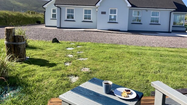 A house with a white exterior and dark roof, a gravel driveway, and a grassy lawn with a picnic table and a plate of food.