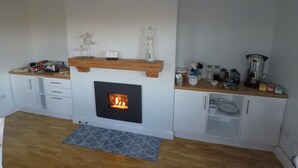 A modern kitchen with a central fireplace, wooden shelves, and white cabinetry.