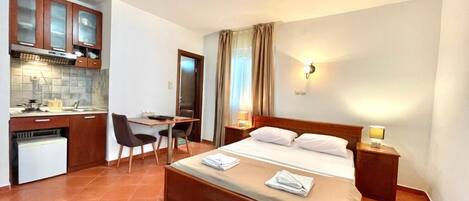 Una habitación de hotel compacta con cama, escritorio, silla y kitchenette.