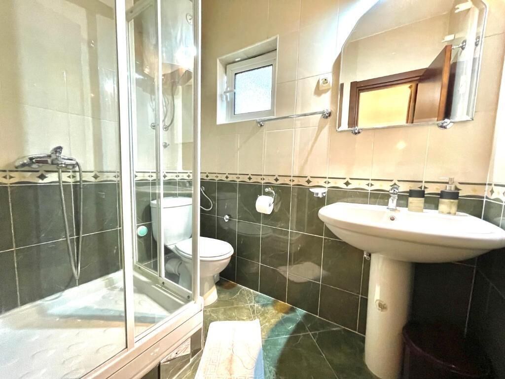 A bathroom with a glass shower enclosure, a toilet, and a sink.