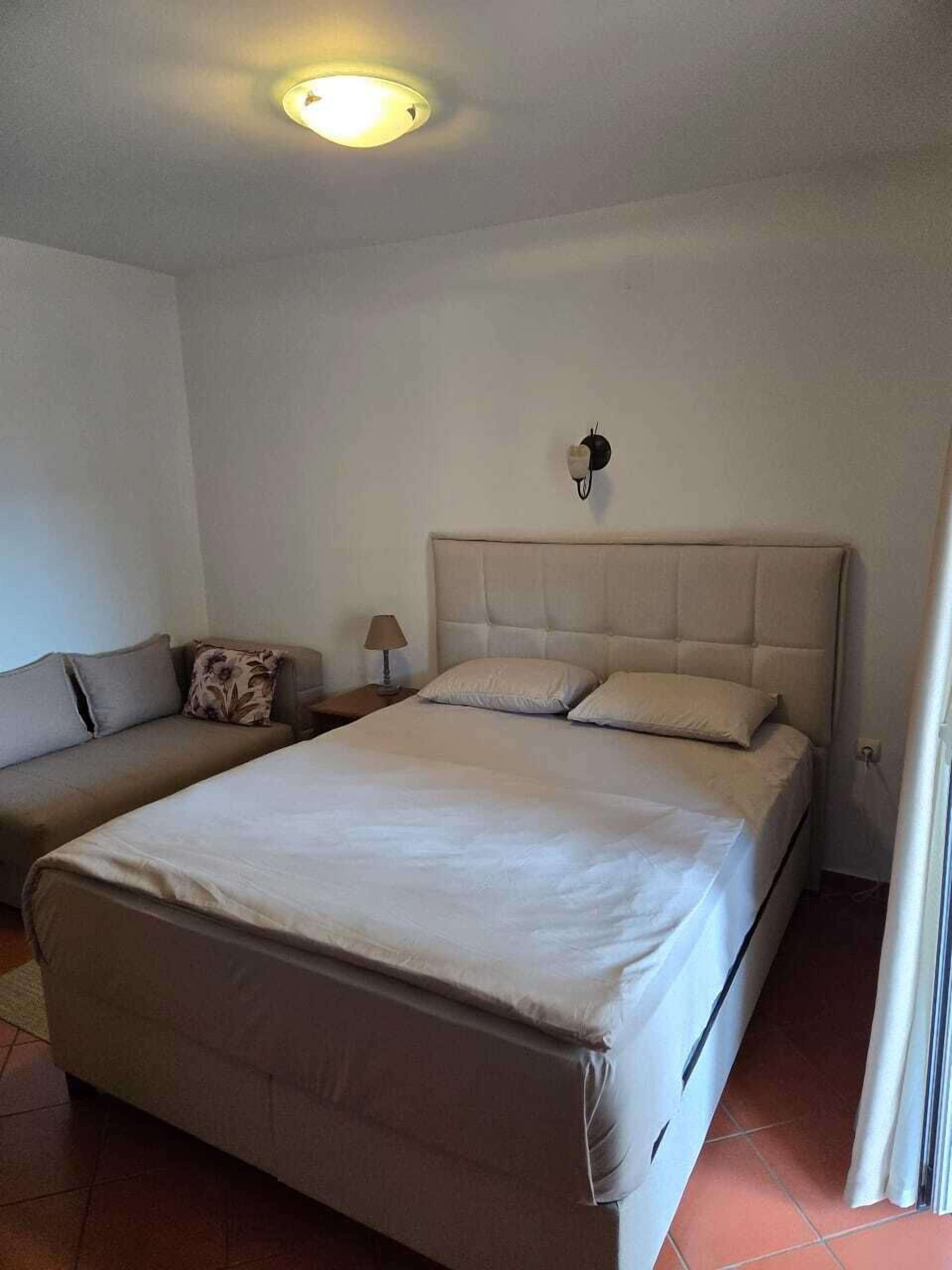Een slaapkamer met een groot bed, een bank, een nachtkastje en een wandlamp.