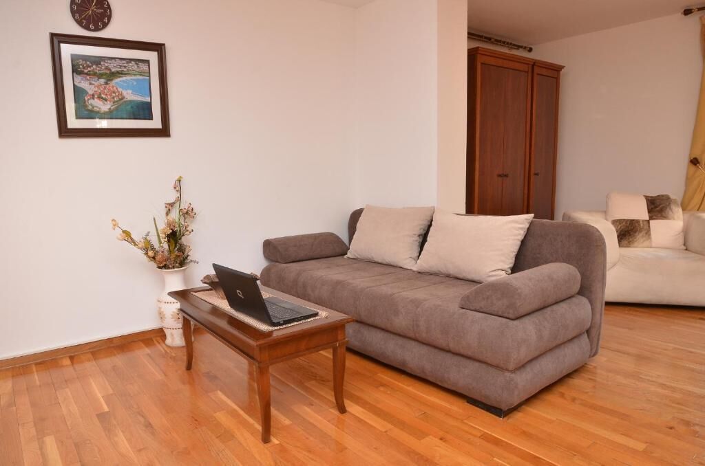 A living room with a brown sofa, a white sofa, a wooden coffee table with a laptop, a vase with flowers, and a framed picture on the wall.