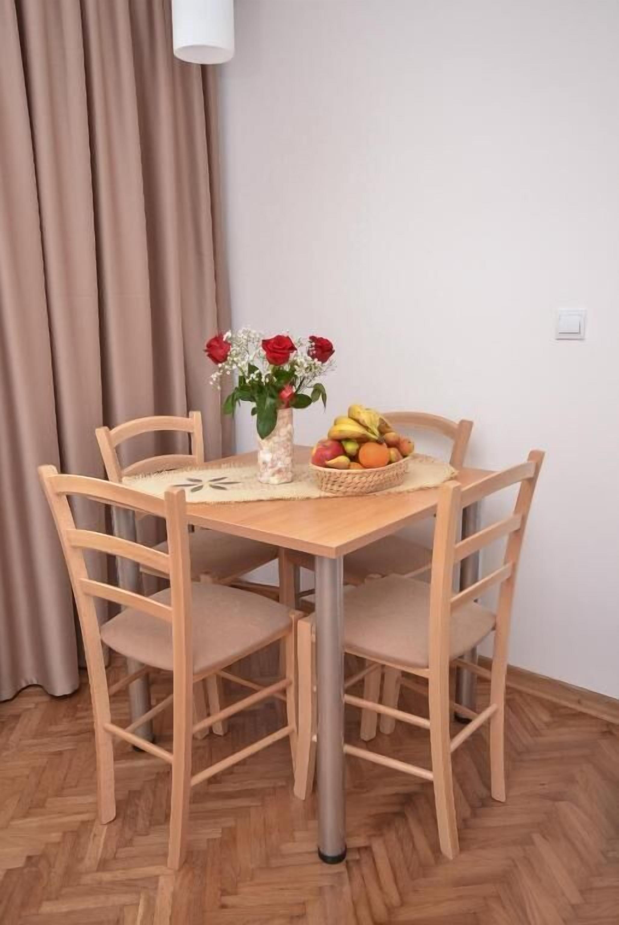 Un tavolo da pranzo con quattro sedie, un vaso di fiori e un cesto di frutta.