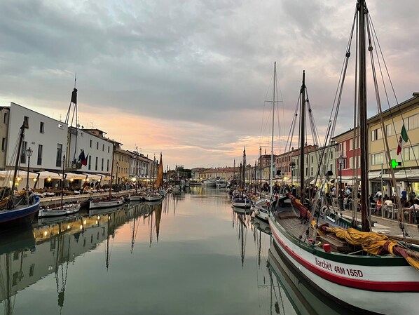 Un port de plaisance où des bateaux sont amarrés le long d’une promenade, entouré de bâtiments dotés d’espaces extérieurs aménagés en terrasses.