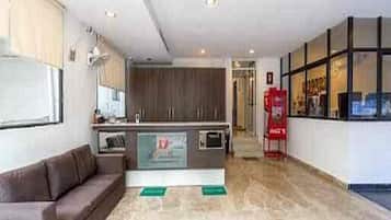 A modern hotel lobby with a brown sofa, a kitchen area, and a red fire extinguisher.