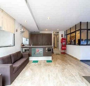A modern hotel lobby with a brown sofa, a kitchen area, and a red fire extinguisher. - Earth Hotel Vadapalani (Chennai)