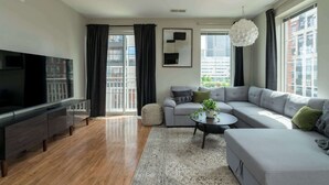 A modern living room with a flat-screen TV, grey sofas, a coffee table, and a large window with curtains. - Luxury Downtown Condo (Columbus)