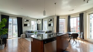 A modern kitchen with a central island, a dining area with chairs, and a living room with a sofa. - Luxury Downtown Condo (Columbus)