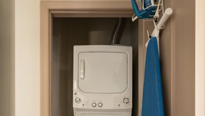A compact laundry room with a washing machine and dryer, a blue ironing board, and a door with a silver handle. - Luxury Downtown Condo (Columbus)