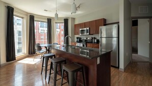 A modern kitchen with a central island, stainless steel appliances, and a view of a red brick building. - Luxury Downtown Condo (Columbus)
