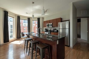 A modern kitchen with a central island, stainless steel appliances, and a view of a red brick building. - Luxury Downtown Condo (Columbus)