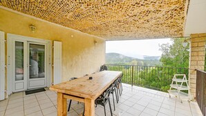 Une table et des chaises en bois sur un balcon donnant sur des collines verdoyantes.